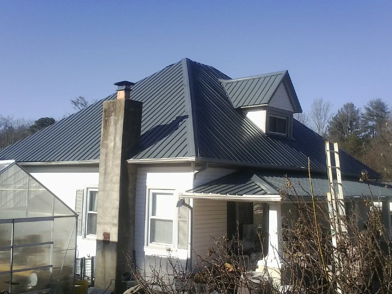 Dark blue standing seam metal roof on a white farmhouse with dormer — Slate & Tile Roof Repair by Roofing Brothers in Cosmopolis