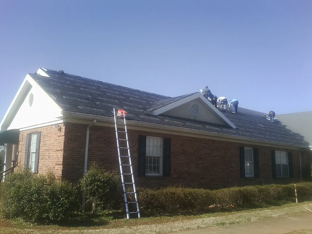 Crew tearing shingles off a brick ranch roof with a ladder set — Metal Roof Repair work by our crew in Cosmopolis