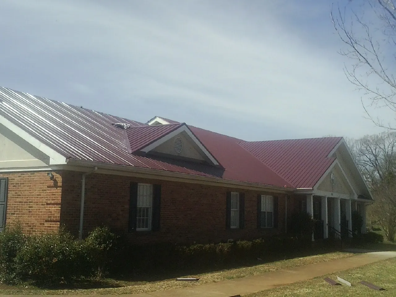 Red metal roof with gabled entries on a long brick building, from a Hail Damage Roof Repair job in Cosmopolis
