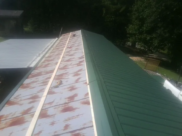 Old rusted panels beside newly installed green metal roofing — Wind Damage Roof Repair by Roofing Brothers in Cosmopolis