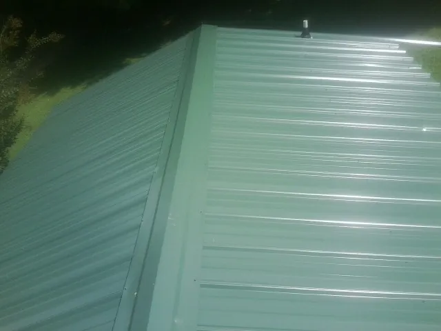 New green metal panels meeting at the ridge of a roof — Flat Roof Repair work by our crew in Cosmopolis