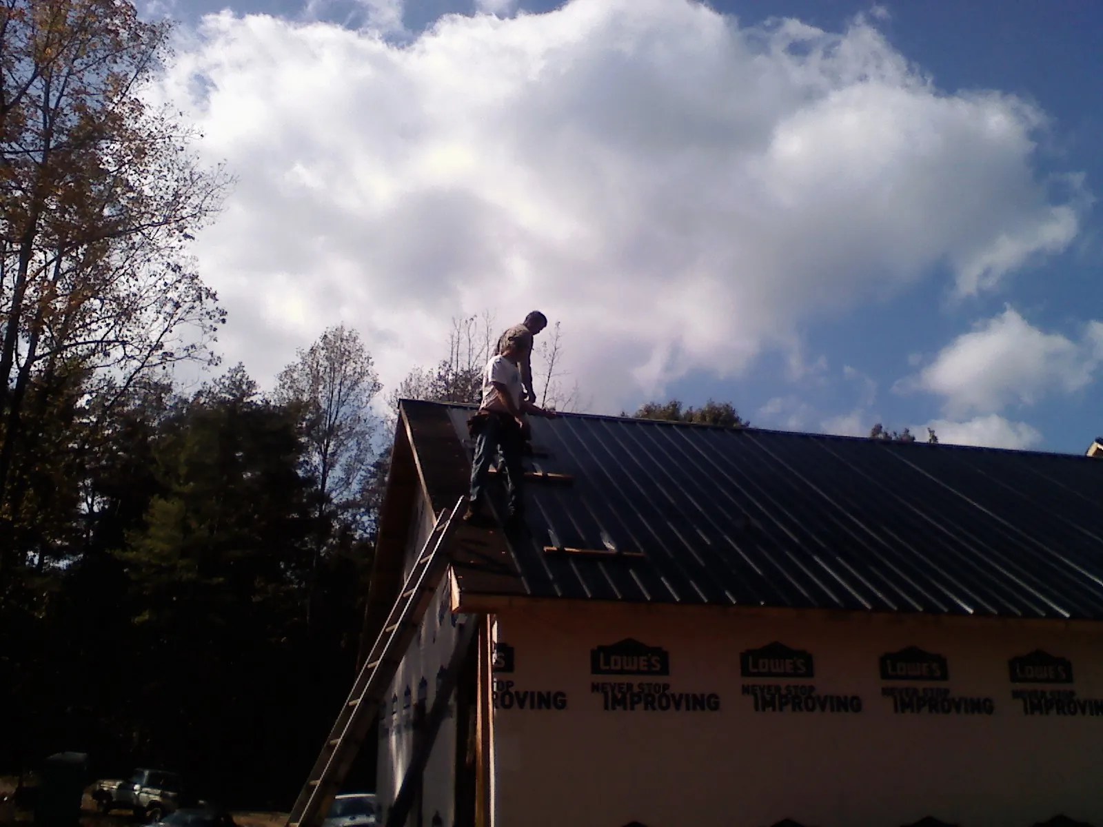 Roofer fastening dark metal panels high against a cloudy sky, from a Roof Inspection job in Cosmopolis