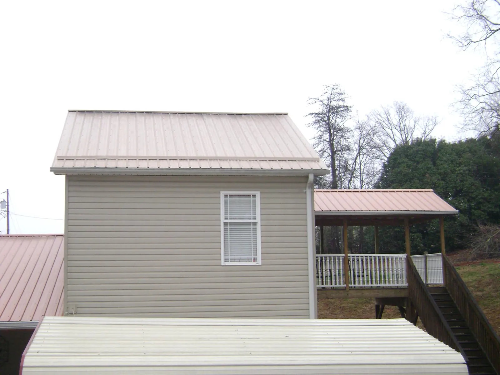 Tan metal roofs on a two story addition and attached porch, from a Roof Replacement job in Cosmopolis